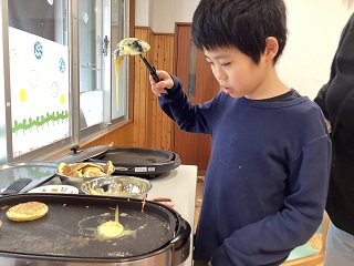 ホットプレートでホットケーキを焼く児童の写真