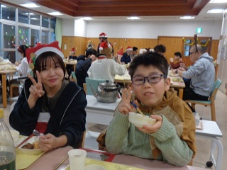 食事を頬張りながらピースする児童と職員