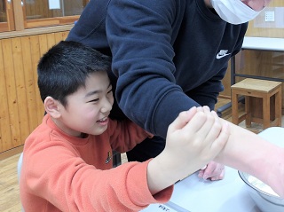 ホットプレートで生地をひっくり返す児童と職員