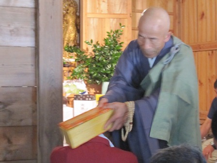 教典で参列者の肩をたたく僧侶の写真